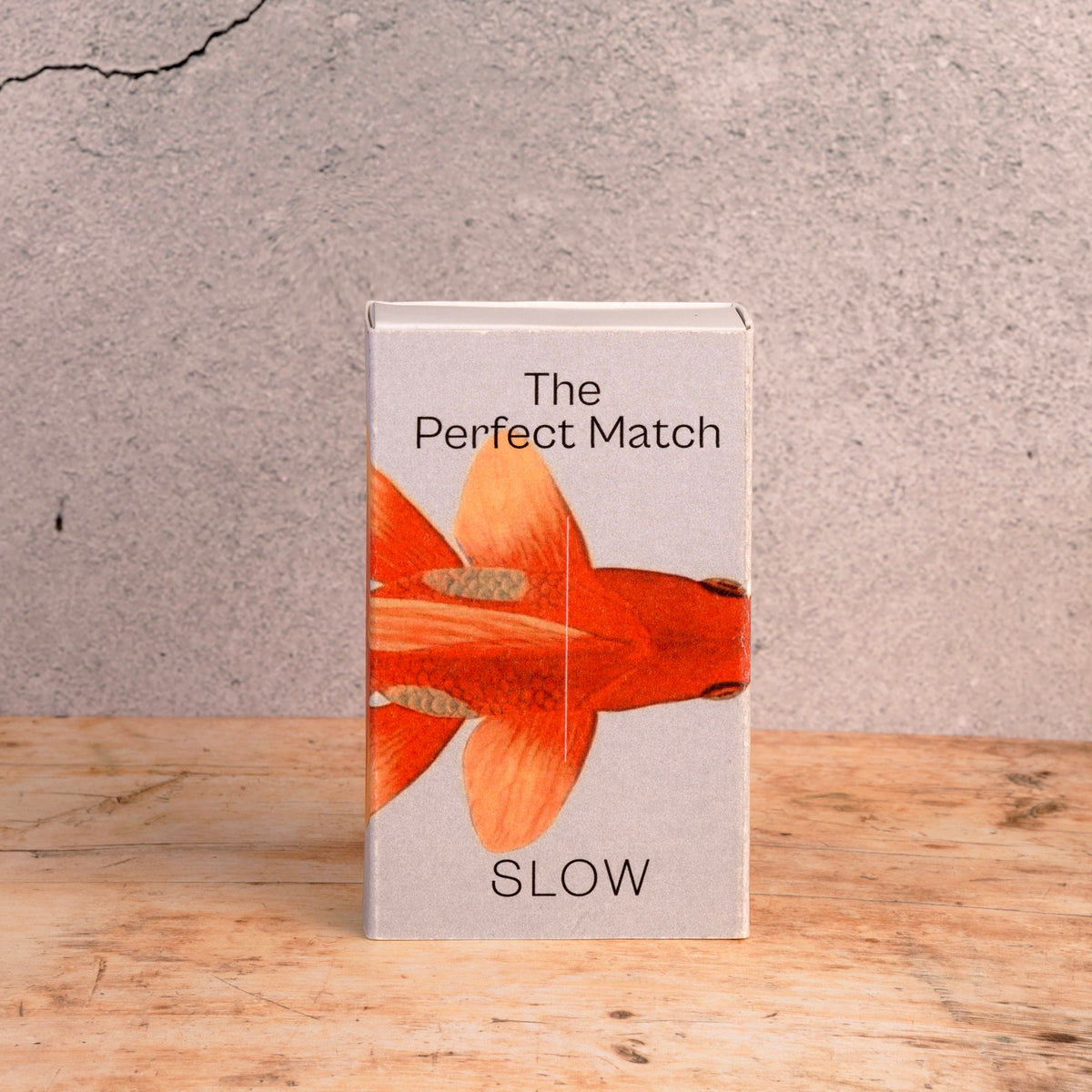 Caixa de 50 fósforos longos da SLOW com ilustração Goldfish, embalada em papel, numa mesa