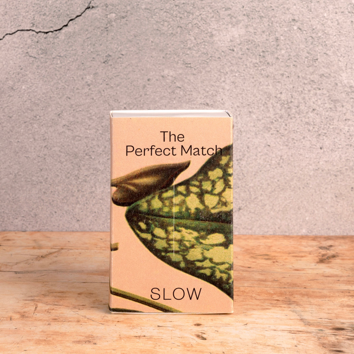 Caixa de 50 fósforos longos da SLOW com ilustração Monstera, embalada em papel, numa mesa