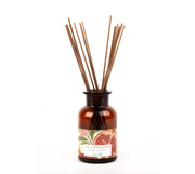 Difusor de varetas em vidro ambar, de nome Granatum da SLOW, e aroma de citronela e romã em óleos essenciais. Etiqueta ilustrada com motivos vegetais e vareta colocadas no vidro em posição de uso.