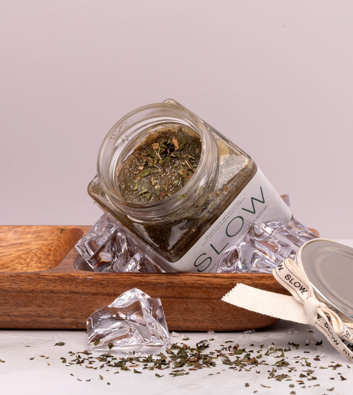 Esfoliante corporal de sal marinho, cristais de menta e hortelã-pimenta, da SLOW, feito à mão em Portugal com gelo num prato de madeira com a tampa aberta