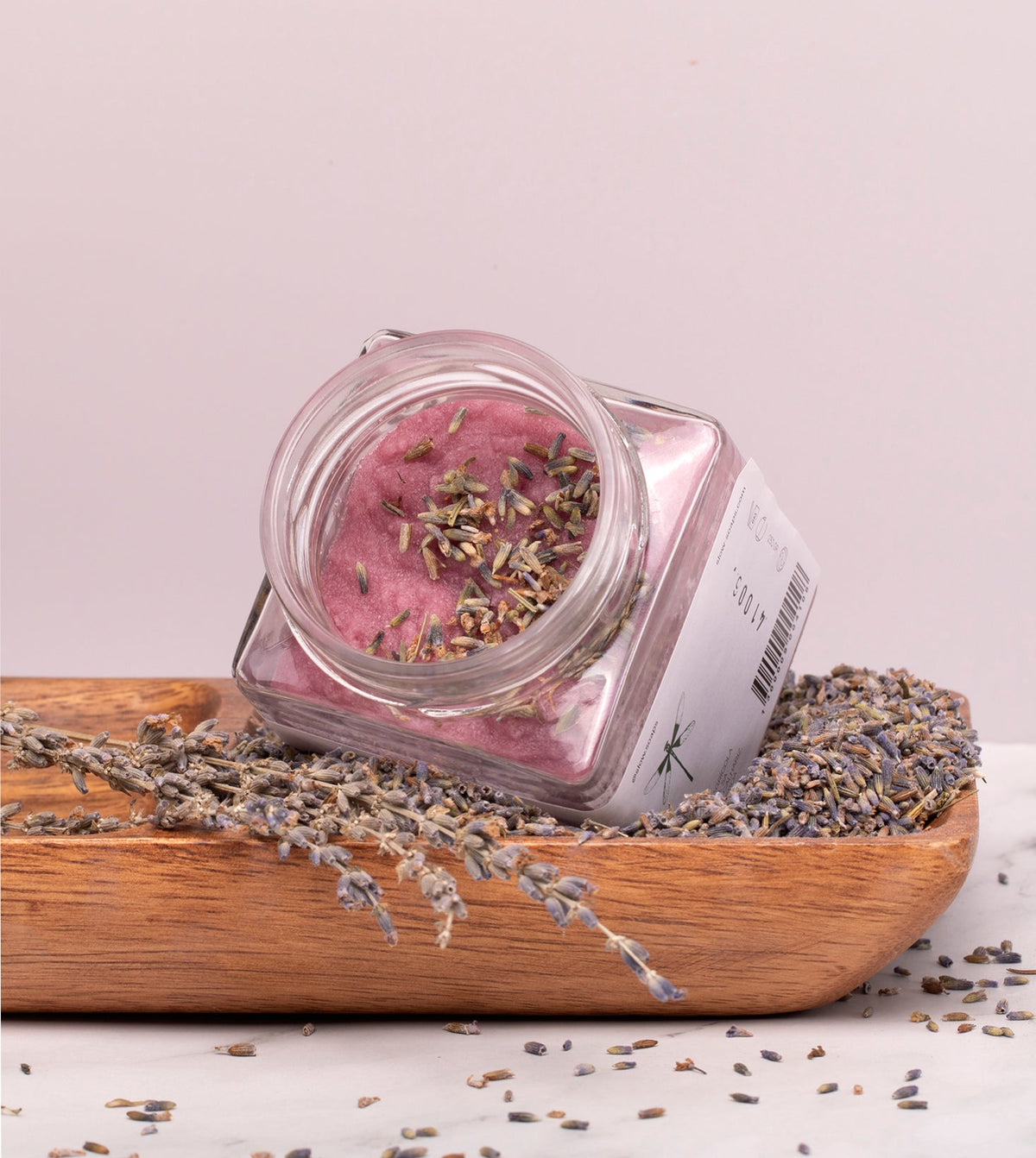 Esfoliante corporal emulsionado de açúcar e óleo essencial de alfazema, da SLOW, feito à mão em Portugal, num prato de madeira e sementes de alfazema, lavanda e tampa aberta