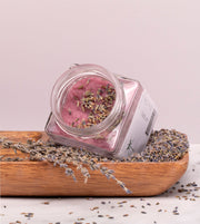 Esfoliante corporal emulsionado de açúcar e óleo essencial de alfazema, da SLOW, feito à mão em Portugal, num prato de madeira e sementes de alfazema, lavanda e tampa aberta